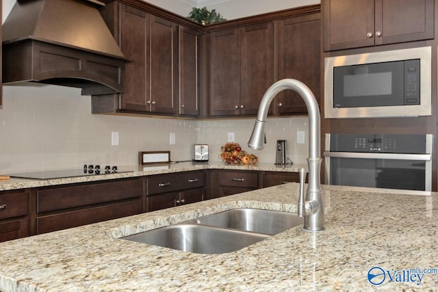 kitchen featuring stainless steel appliances, light stone countertops, premium range hood, and decorative backsplash