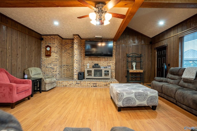 living room featuring lofted ceiling with beams, light wood-type flooring, wooden walls, and ceiling fan