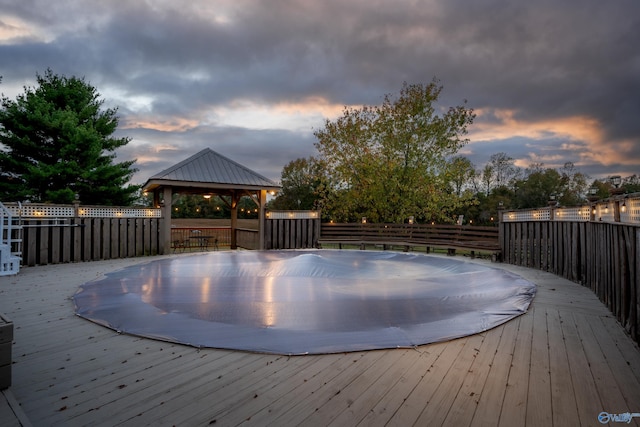 pool at dusk with a deck and a gazebo