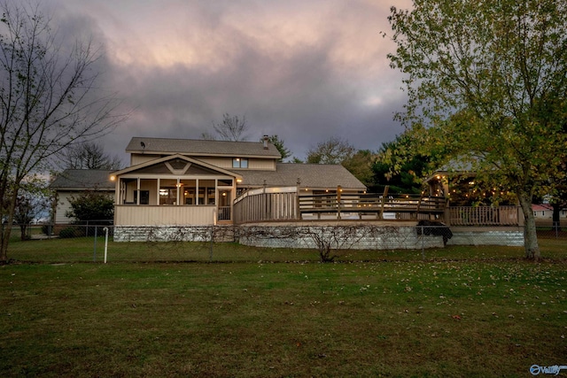 back house at dusk featuring a lawn and a sunroom