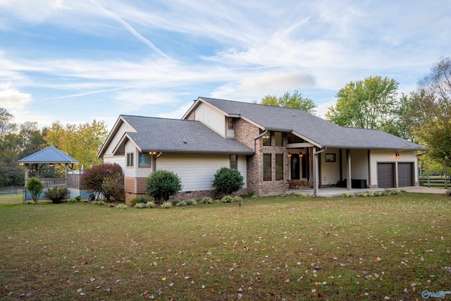 rear view of property with a garage, a yard, and a gazebo