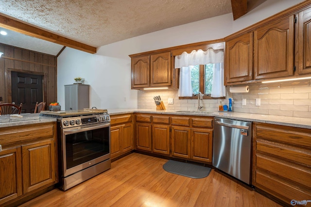 kitchen featuring decorative backsplash, a textured ceiling, sink, light wood-type flooring, and appliances with stainless steel finishes