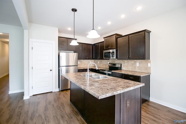 kitchen featuring a kitchen island with sink, dark brown cabinets, stainless steel appliances, tasteful backsplash, and decorative light fixtures