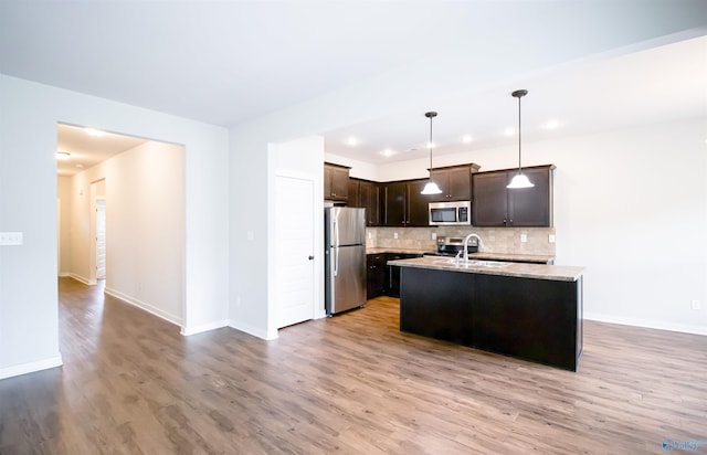 kitchen featuring appliances with stainless steel finishes, tasteful backsplash, hanging light fixtures, dark brown cabinetry, and a center island with sink