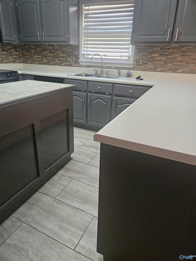 kitchen featuring backsplash, light tile patterned flooring, sink, and gray cabinetry