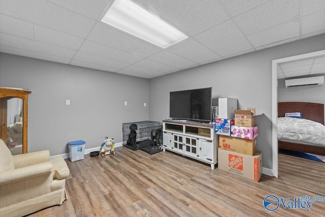 living room featuring a wall mounted AC, light hardwood / wood-style floors, and a drop ceiling