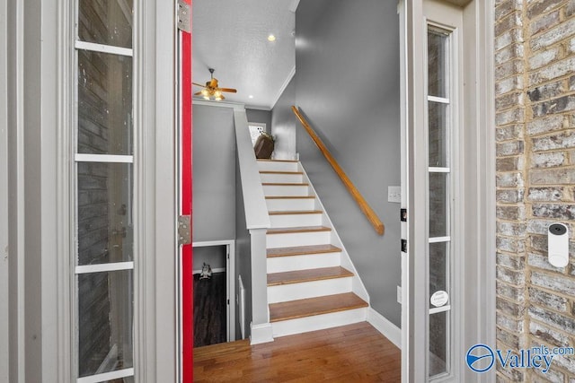 stairs with crown molding, wood-type flooring, ceiling fan, and a textured ceiling