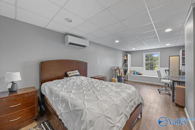 bedroom featuring wood-type flooring, a drop ceiling, and a wall unit AC