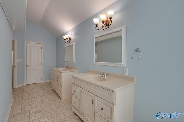 bathroom featuring stone tile floors, baseboards, a sink, vaulted ceiling, and two vanities