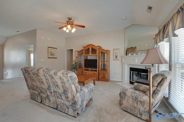 living area with lofted ceiling, visible vents, a fireplace with flush hearth, light carpet, and ceiling fan