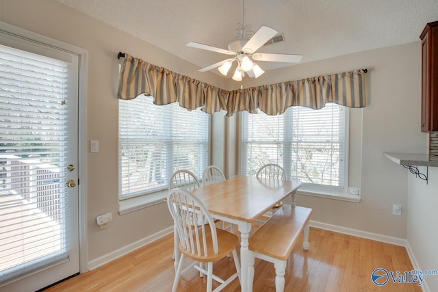 dining area featuring light wood-style floors, baseboards, a ceiling fan, and a textured ceiling