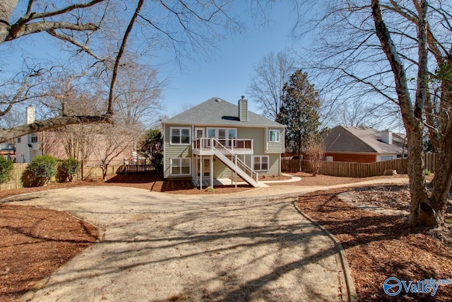 view of front of property featuring fence, stairs, driveway, a wooden deck, and a chimney