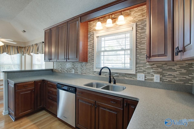 kitchen with a textured ceiling, lofted ceiling, a peninsula, a sink, and stainless steel dishwasher