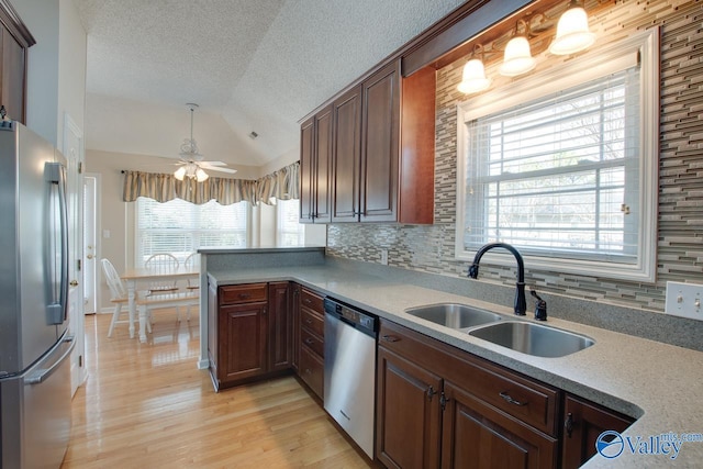 kitchen featuring light wood finished floors, decorative backsplash, appliances with stainless steel finishes, vaulted ceiling, and a sink