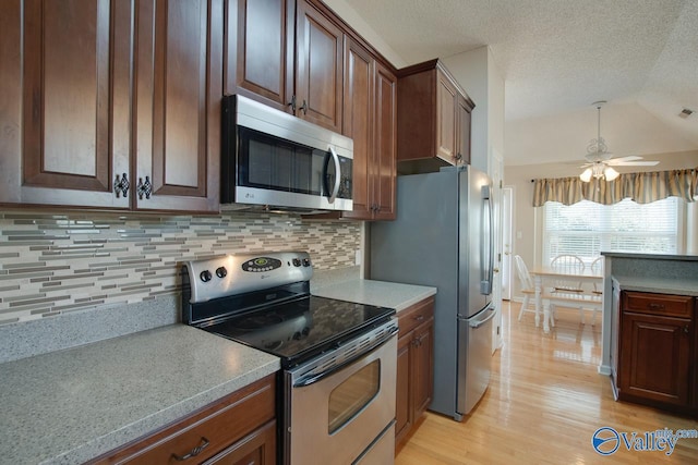 kitchen featuring light wood finished floors, stainless steel appliances, tasteful backsplash, light countertops, and vaulted ceiling