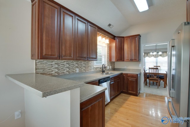 kitchen featuring appliances with stainless steel finishes, vaulted ceiling, a sink, light wood-type flooring, and a peninsula