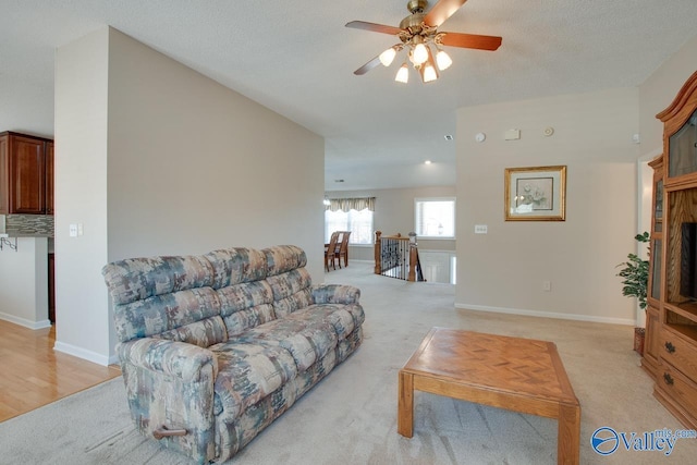 living room featuring a ceiling fan, light colored carpet, a textured ceiling, and baseboards