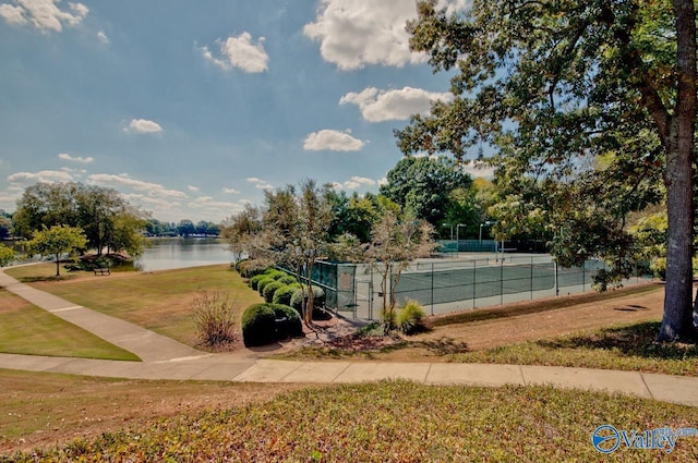 view of tennis court featuring a water view, fence, and a yard