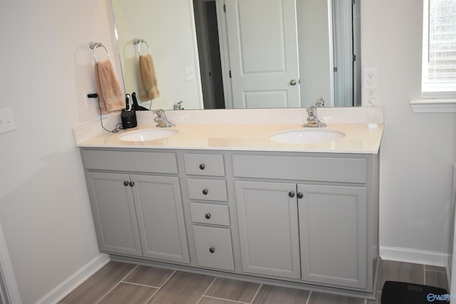 full bath featuring double vanity, wood tiled floor, a sink, and baseboards