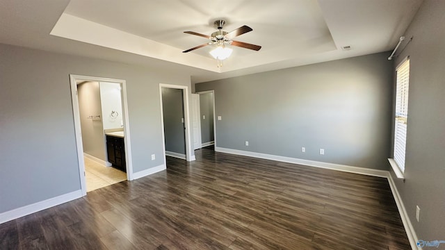 unfurnished bedroom with a raised ceiling, dark hardwood / wood-style floors, connected bathroom, and ceiling fan