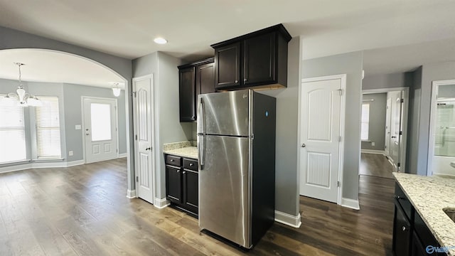 kitchen featuring light stone counters, dark hardwood / wood-style floors, stainless steel fridge, and decorative light fixtures