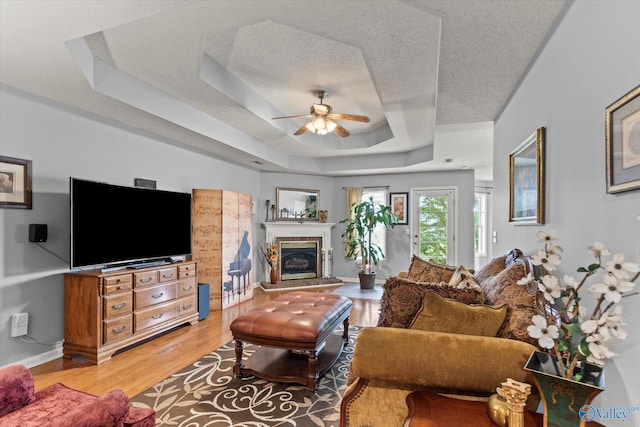194 Bonaire Dr, Huntsville, AL 35811 - living area featuring ceiling fan, a raised ceiling, a glass covered fireplace, light wood-style floors, and a textured ceiling