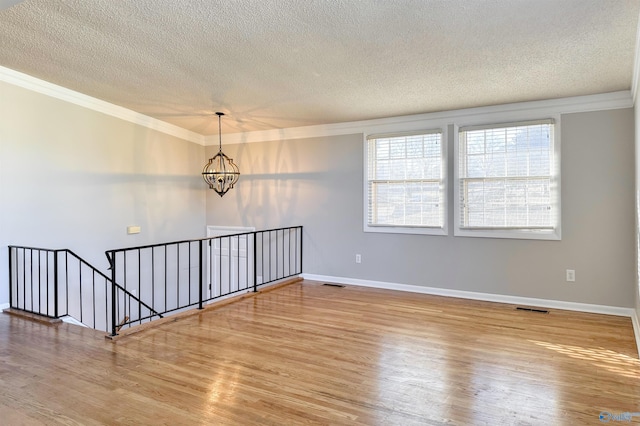 unfurnished room with hardwood / wood-style floors, a textured ceiling, an inviting chandelier, and crown molding