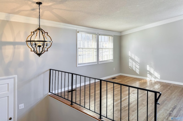 stairs featuring hardwood / wood-style flooring, ornamental molding, a textured ceiling, and an inviting chandelier