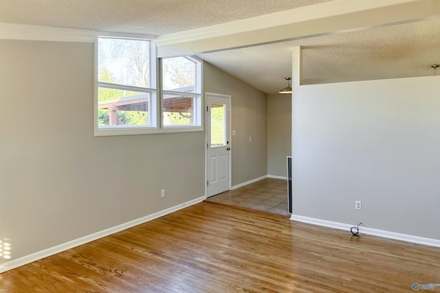 unfurnished room with vaulted ceiling with beams, light hardwood / wood-style floors, and a textured ceiling