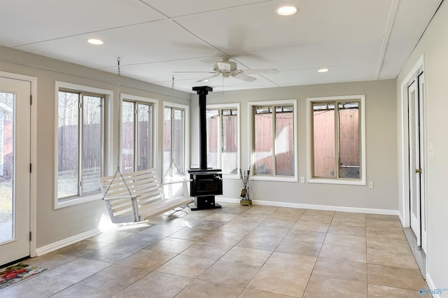 unfurnished sunroom with a wood stove, a wealth of natural light, and ceiling fan