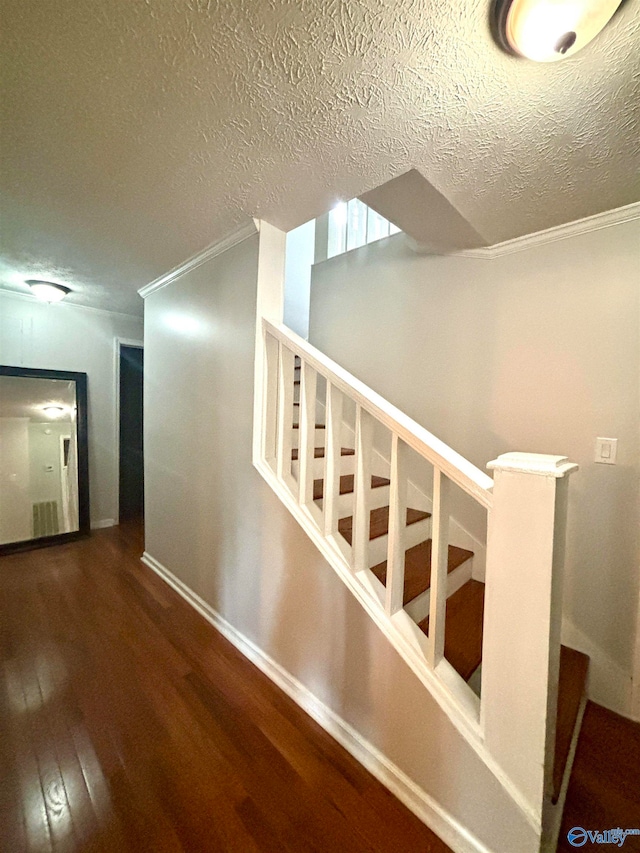 stairway with a textured ceiling, ornamental molding, and wood-type flooring