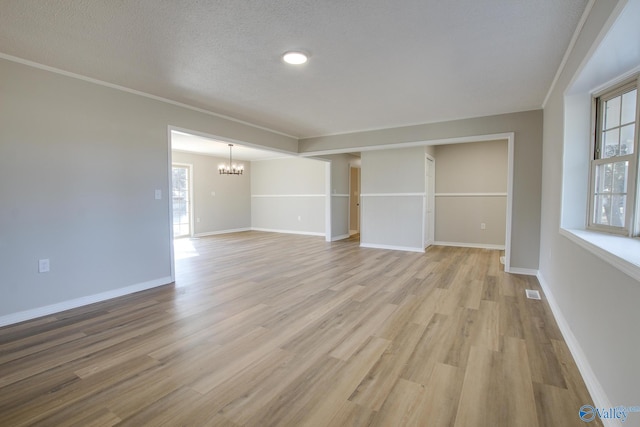 empty room featuring light hardwood / wood-style flooring, ornamental molding, a chandelier, and a textured ceiling