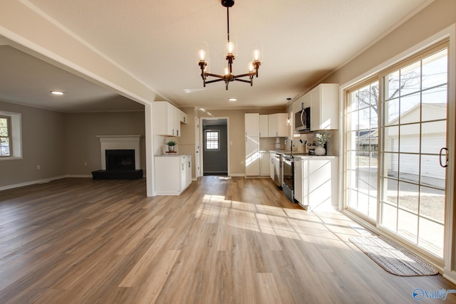 kitchen featuring pendant lighting, light hardwood / wood-style flooring, stainless steel appliances, tasteful backsplash, and white cabinets