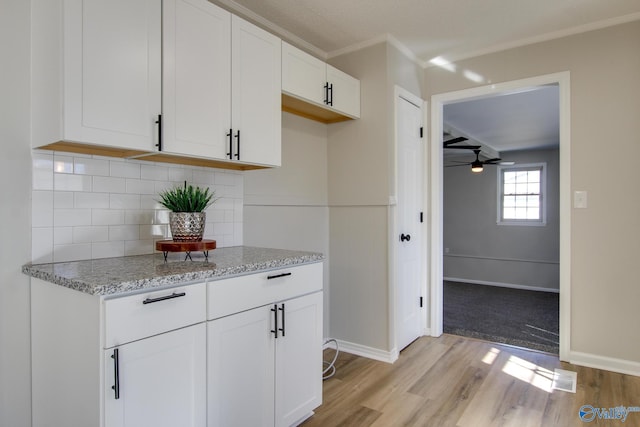 kitchen featuring white cabinetry, tasteful backsplash, light stone counters, ornamental molding, and light hardwood / wood-style floors