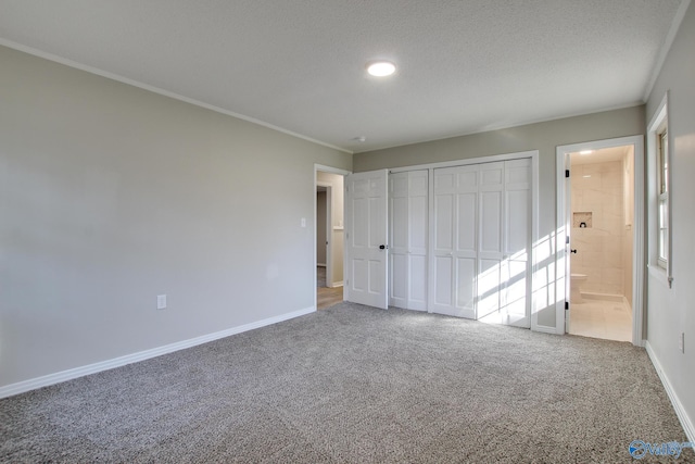 unfurnished bedroom with ensuite bathroom, a textured ceiling, ornamental molding, carpet floors, and a closet