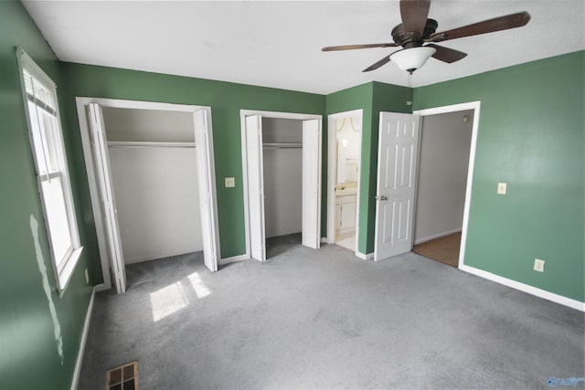 unfurnished bedroom featuring carpet floors, visible vents, baseboards, and two closets