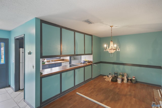 kitchen featuring light wood finished floors, visible vents, an inviting chandelier, a textured ceiling, and a sink