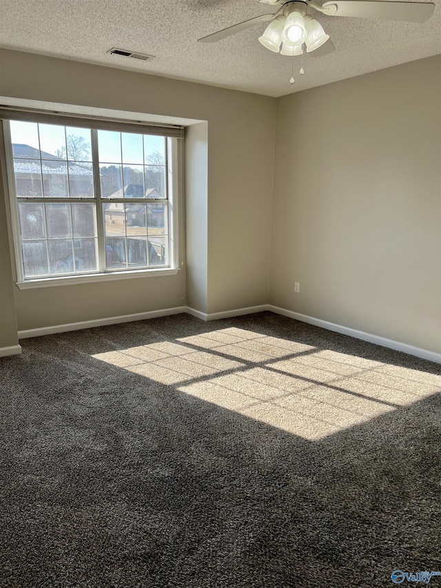 spare room featuring ceiling fan, dark carpet, and a textured ceiling