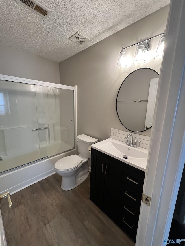 full bathroom with a textured ceiling, vanity, shower / bath combination with glass door, wood-type flooring, and toilet