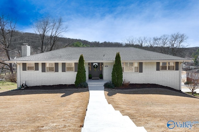 ranch-style home featuring brick siding, a chimney, and roof with shingles