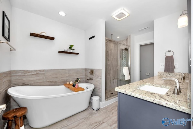 full bath featuring tile walls, visible vents, a stall shower, vanity, and a freestanding tub