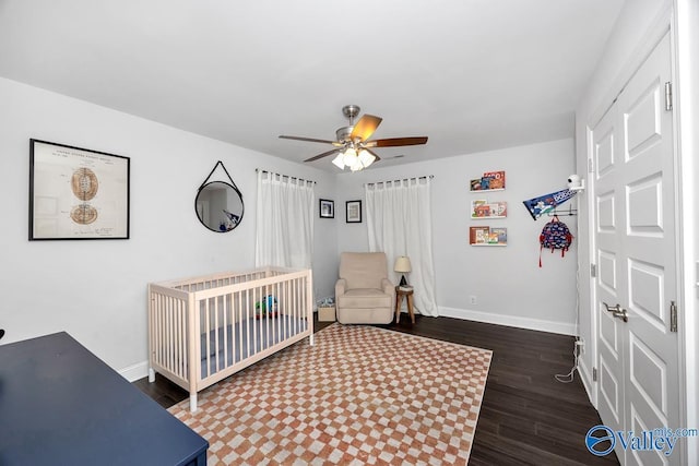 bedroom featuring a ceiling fan, a crib, baseboards, and wood finished floors