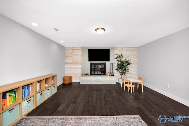 living room with a brick fireplace, visible vents, baseboards, and wood finished floors