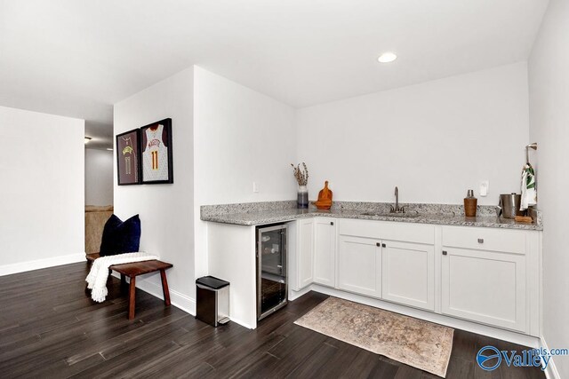 bar featuring dark wood-style floors, a sink, wet bar, beverage cooler, and baseboards