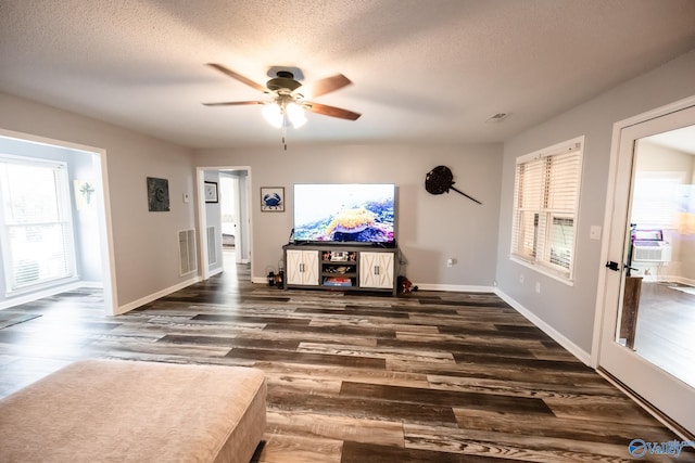 unfurnished living room with a wealth of natural light, visible vents, ceiling fan, and dark wood-style floors