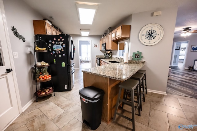 kitchen featuring a peninsula, light stone countertops, black appliances, a kitchen bar, and a sink