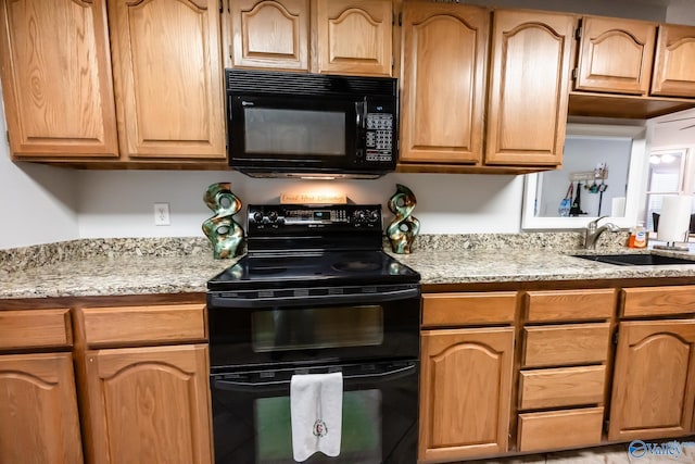 kitchen with light stone countertops, black appliances, light brown cabinets, and a sink