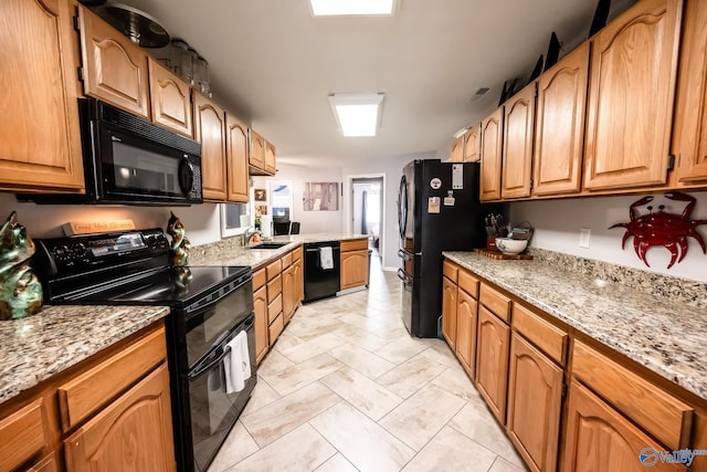 kitchen featuring black appliances, light stone counters, brown cabinets, and a sink