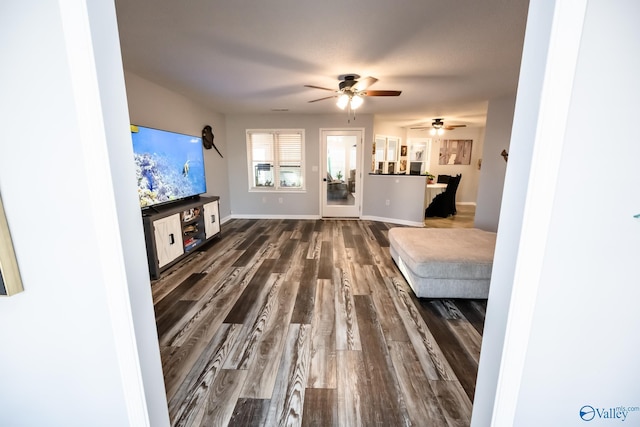 unfurnished living room with baseboards, a ceiling fan, and dark wood-style flooring