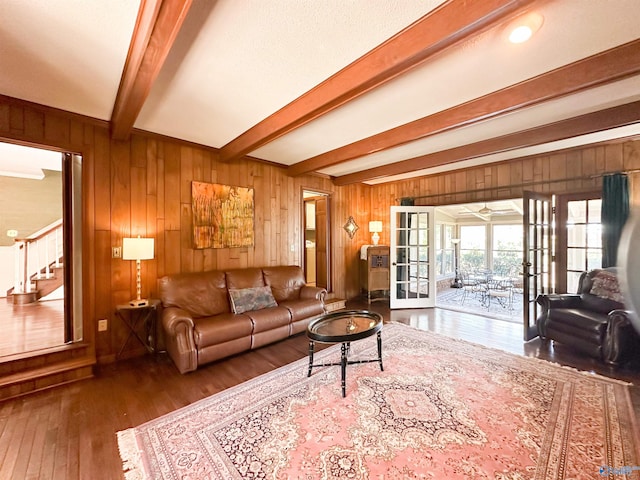 living area featuring wooden walls, stairs, wood finished floors, beam ceiling, and french doors